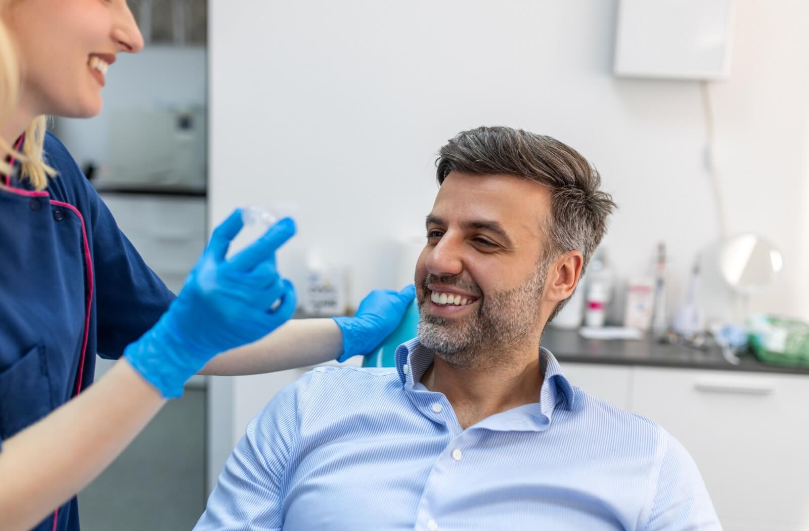 A smiling person at the dentist is given Invisalign aligners from a dental professional.