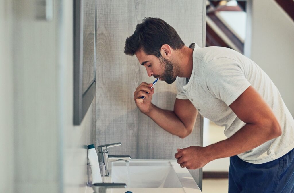 A person brushes his teeth in the bathroom mirror as part of his daily oral hygiene routine.