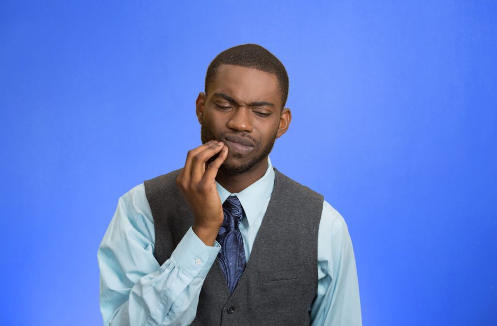 A man standing in front of a purple background, holding his lip due to a lip injury.