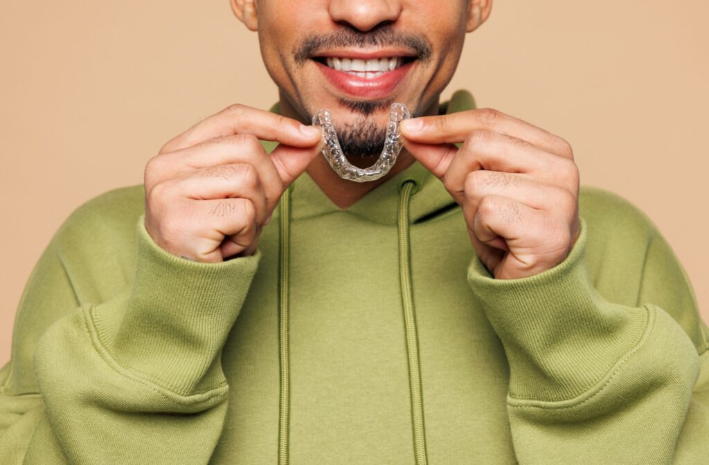 A person cheerfully holds their Invisalign aligner tray.
