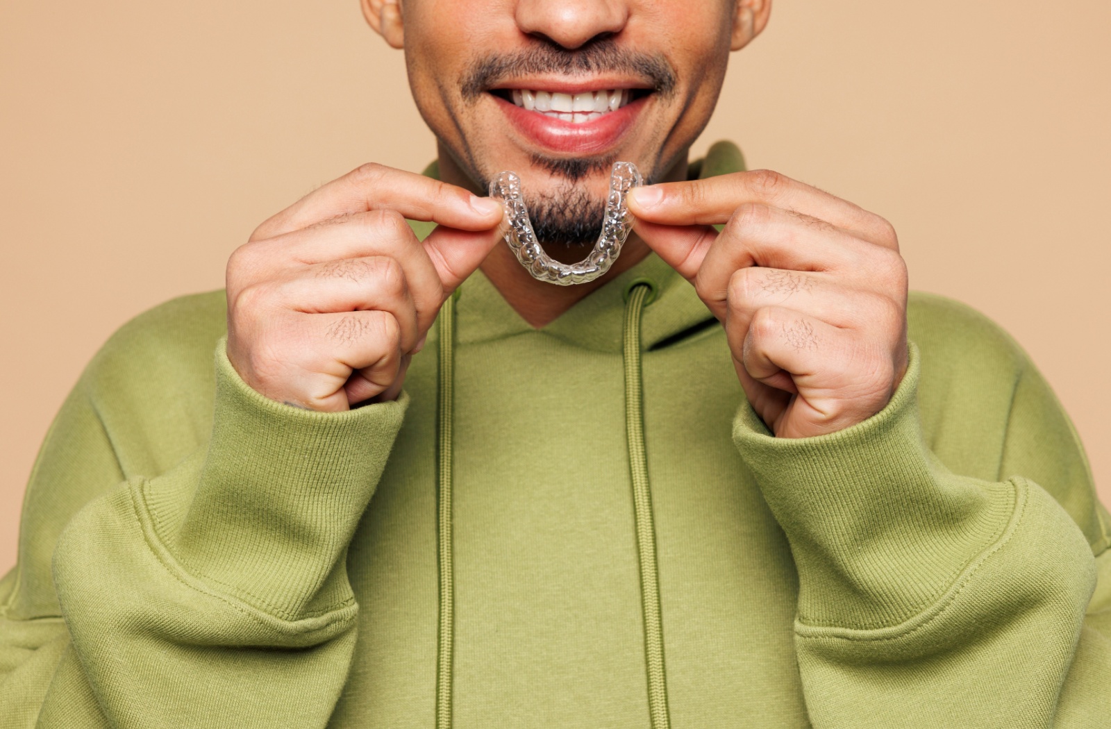 A person cheerfully holds their Invisalign aligner tray.