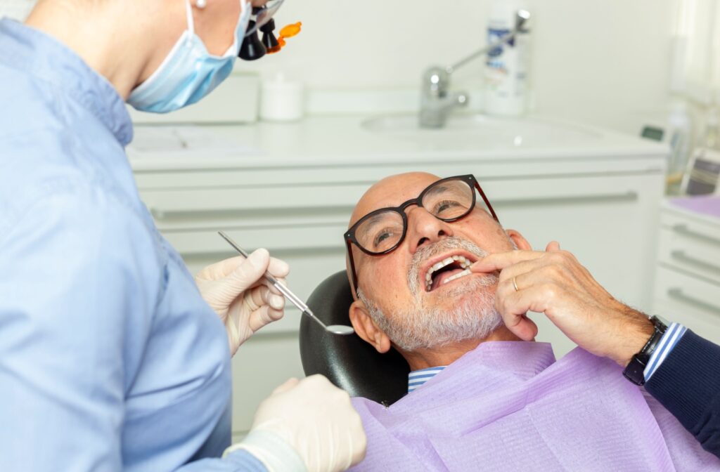 A patient at a dental exam, point to their mouth to explain where they feel pain around their dental bridge to the dentist.