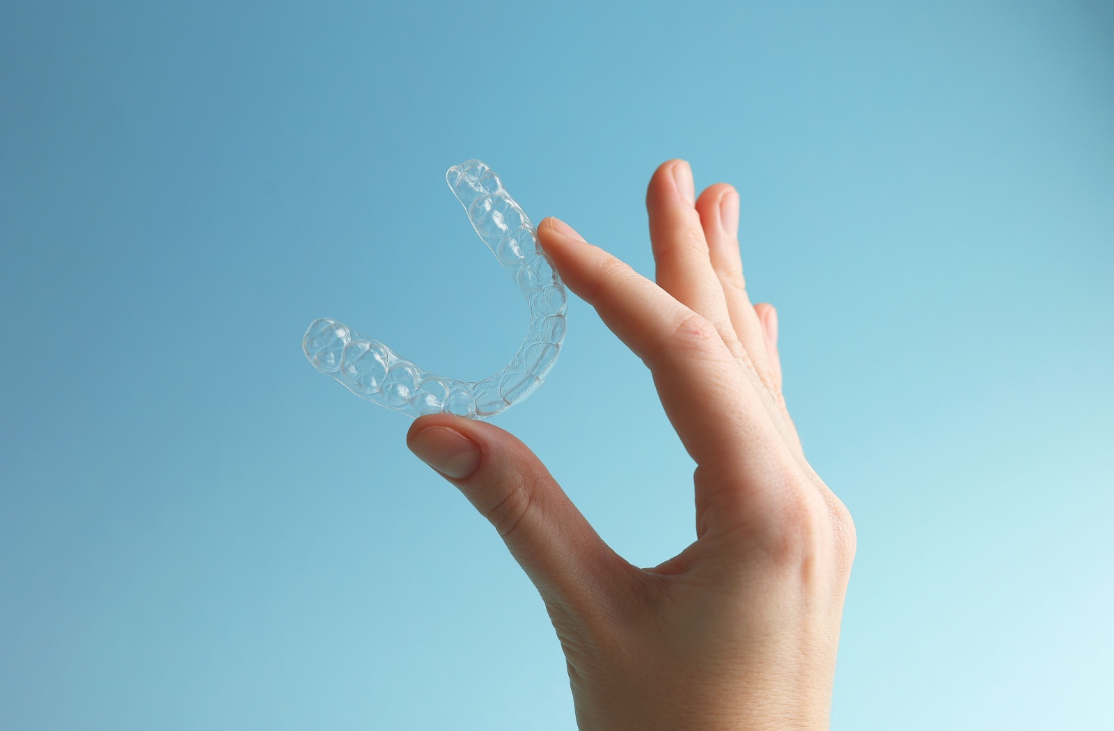 A hand holding up an Invisalign aligner in front of a blue background.