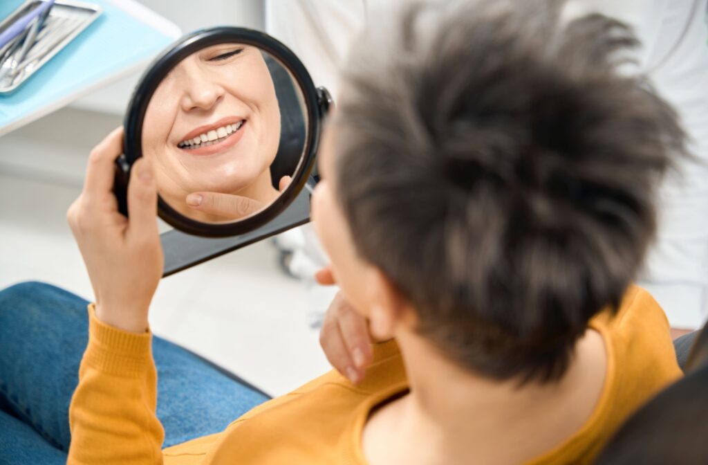 A dental patient looking in a handheld mirror to see their smile after having a dental implant procedure.