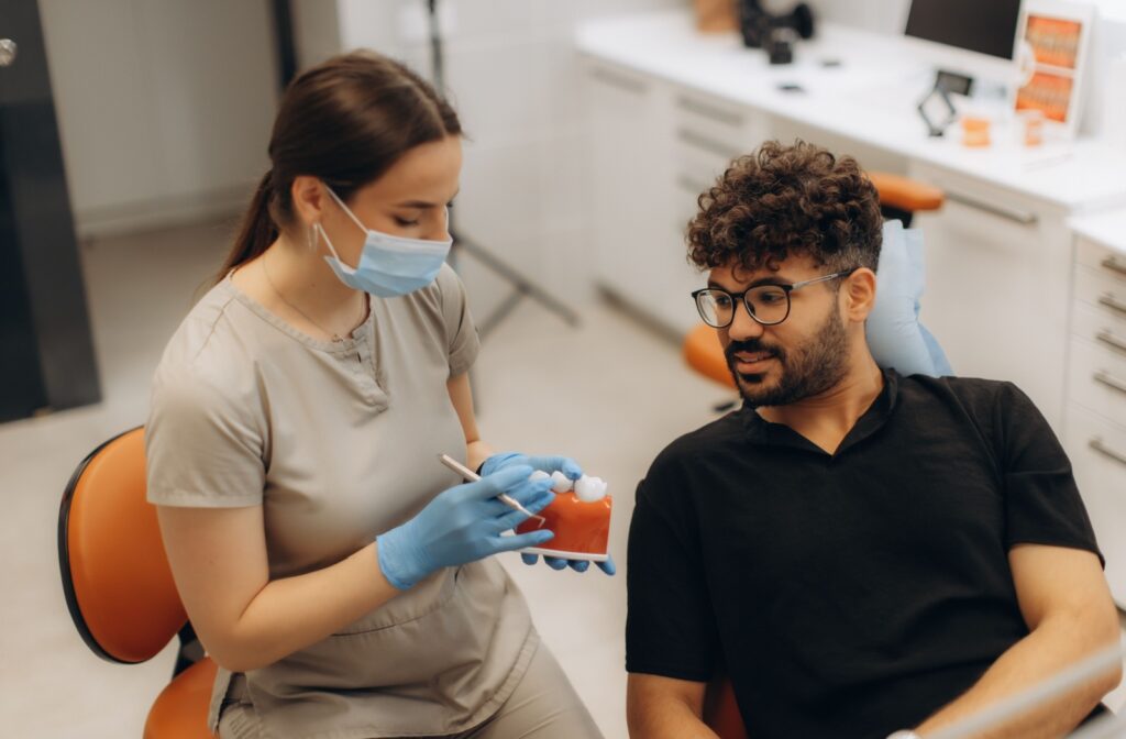 A dentist holding a 3D model of teeth, showing a patient the final step of the dental implant procedure, attaching a the new tooth.