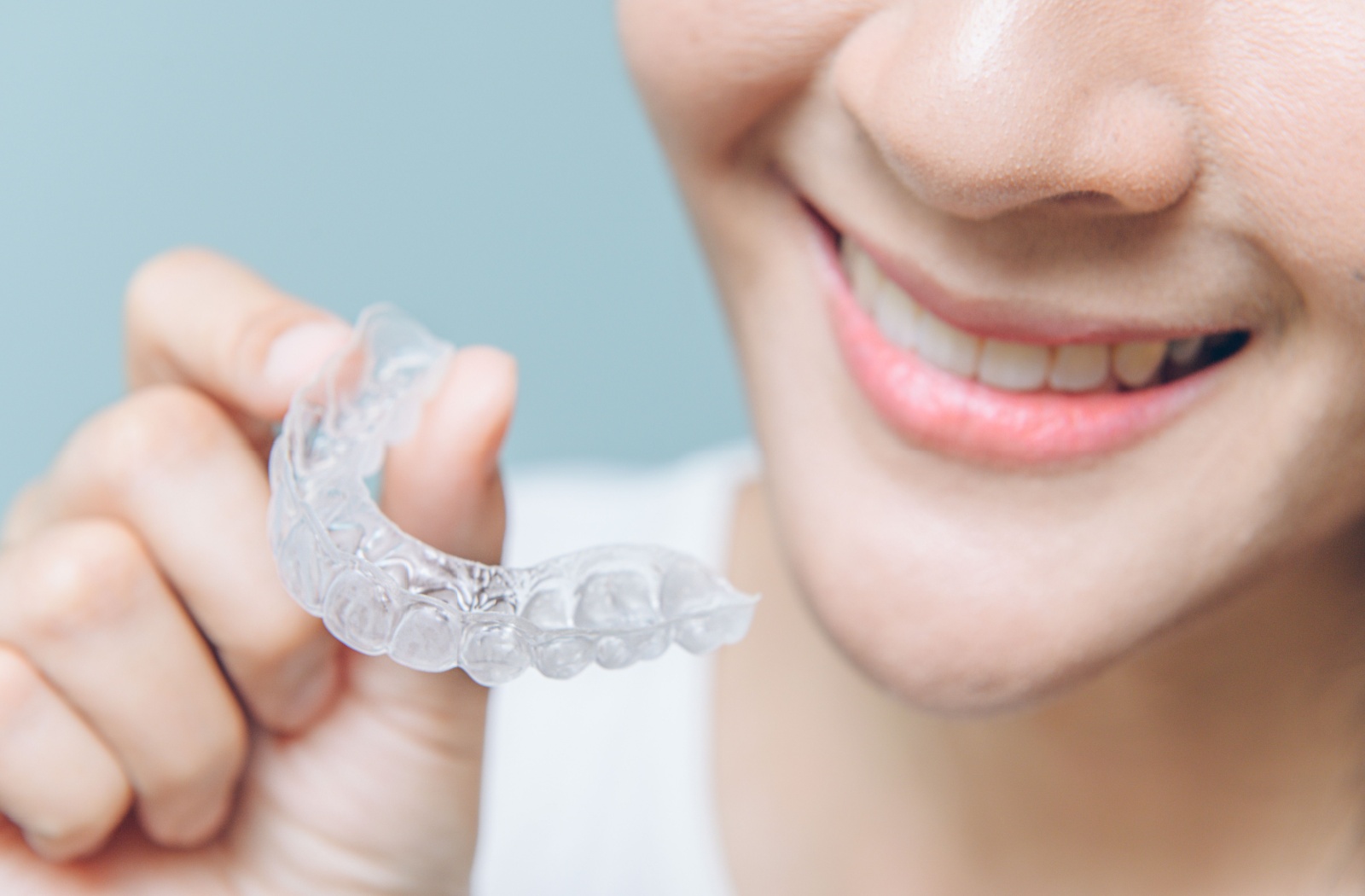 A person smiling while holding Invisalign tray up to their mouth
