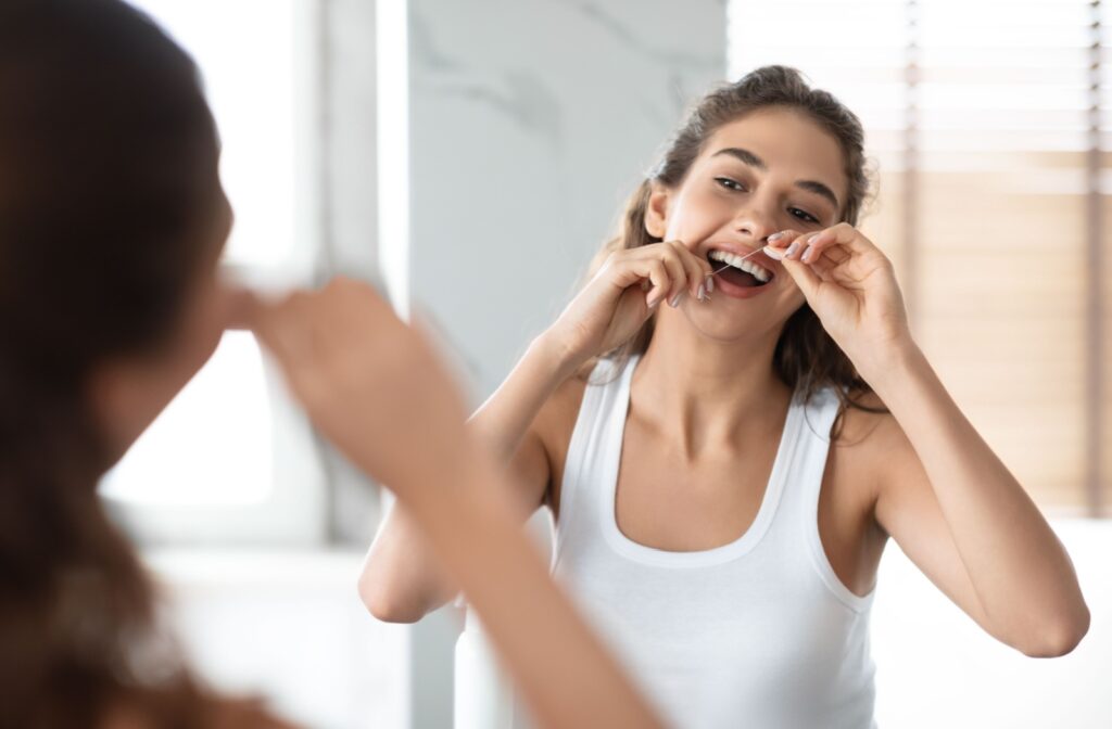 A person looking in the mirror as hey floss in between their teeth for optimal hygiene