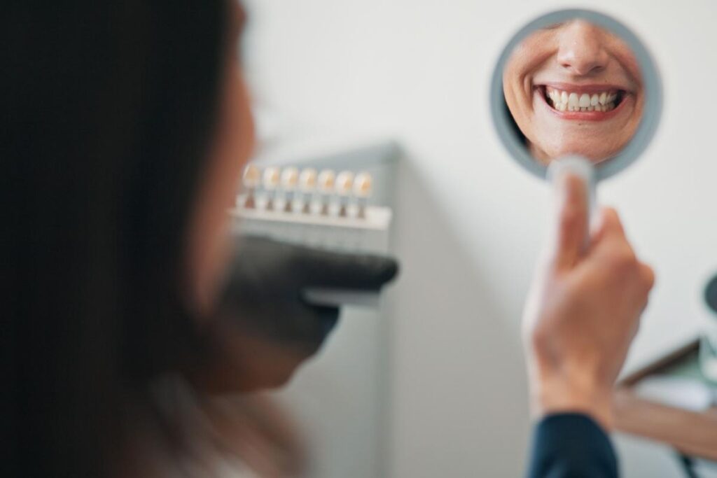 a person looking in a small mirror and smiling while at the dentist